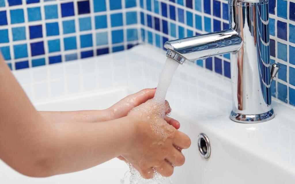 A person washing their hands under a running water tap
