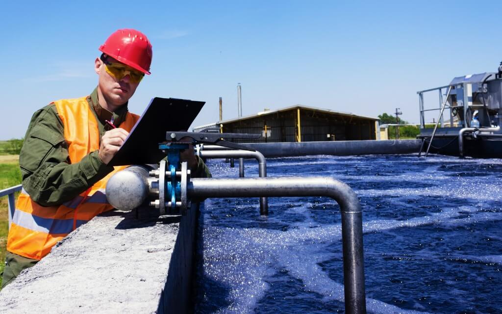 A person in a hard hat writing on a clipboard at water treatment facility